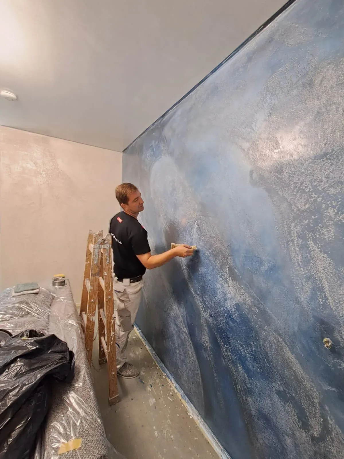 Senad Bećić spachtelt eine künstlerische Wand in tiefem Blau